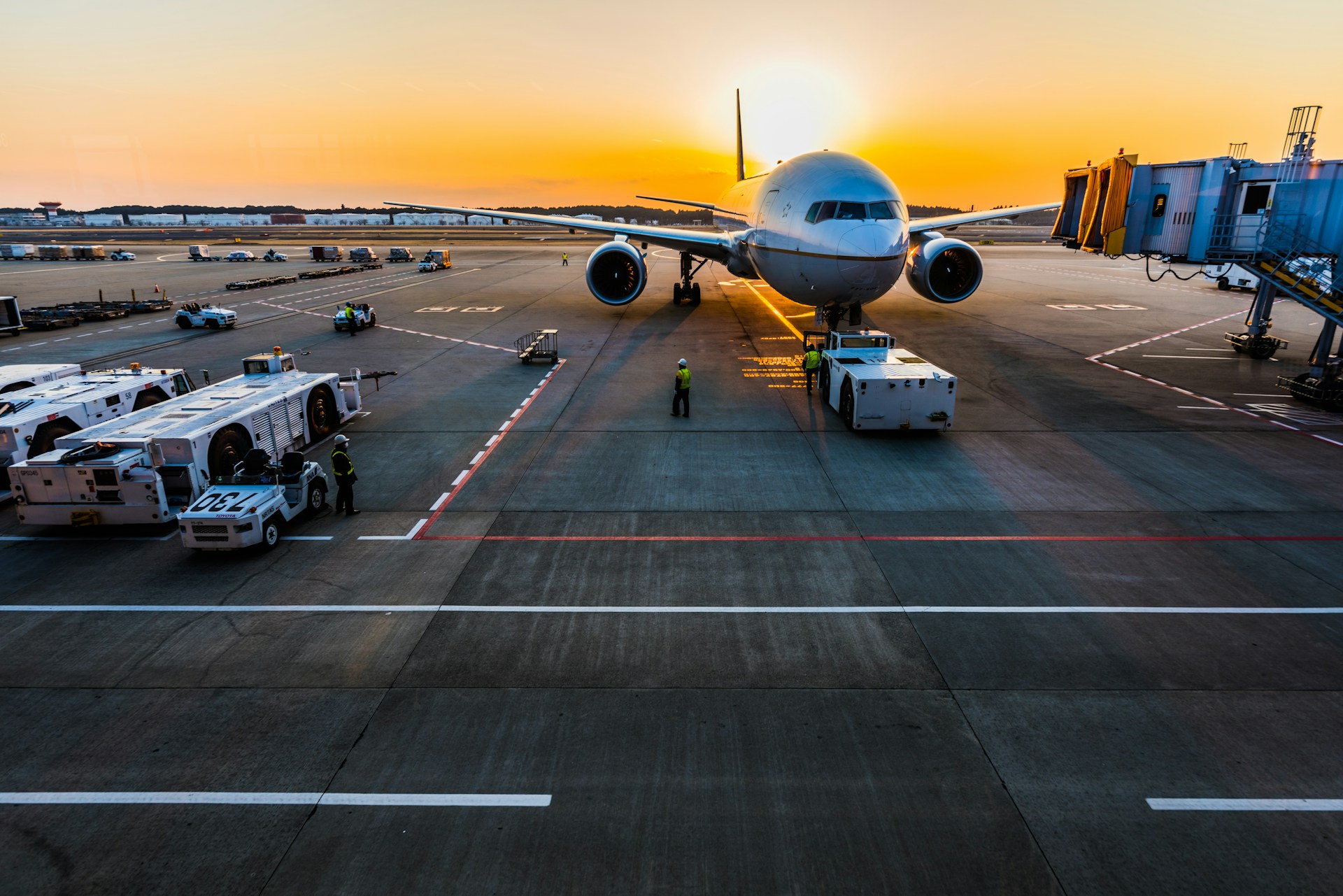 A large passenger plane near a gate on an airport tarmac, with the sun setting in the background